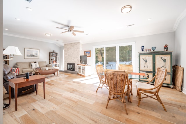 dining room featuring visible vents, ceiling fan, light wood-style flooring, ornamental molding, and a stone fireplace