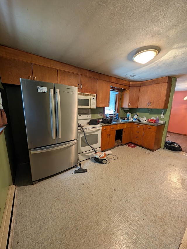 kitchen with a sink, white appliances, brown cabinets, and a textured ceiling