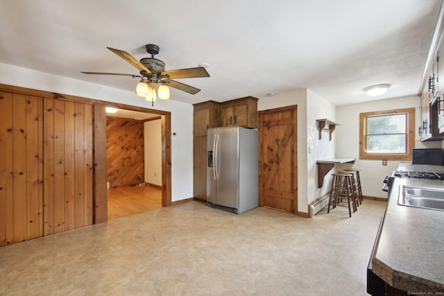 kitchen featuring wooden walls, dark countertops, a baseboard heating unit, stainless steel refrigerator with ice dispenser, and a sink