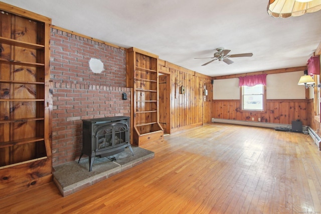 unfurnished living room featuring a wood stove, wood walls, wood-type flooring, and a ceiling fan