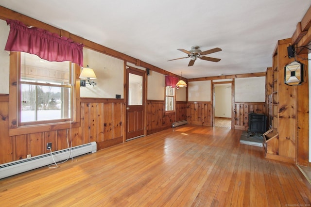 unfurnished living room with a baseboard heating unit, a wood stove, wainscoting, and wood-type flooring