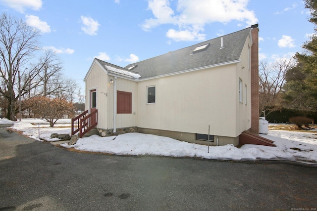 view of front of house featuring entry steps, a chimney, and roof with shingles