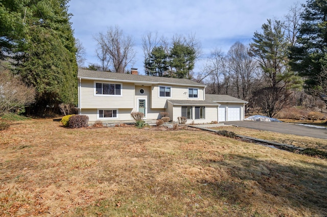 raised ranch with a garage, a front lawn, a chimney, and aphalt driveway