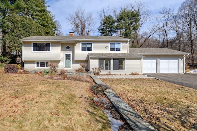 bi-level home featuring a garage, aphalt driveway, a chimney, and a front yard