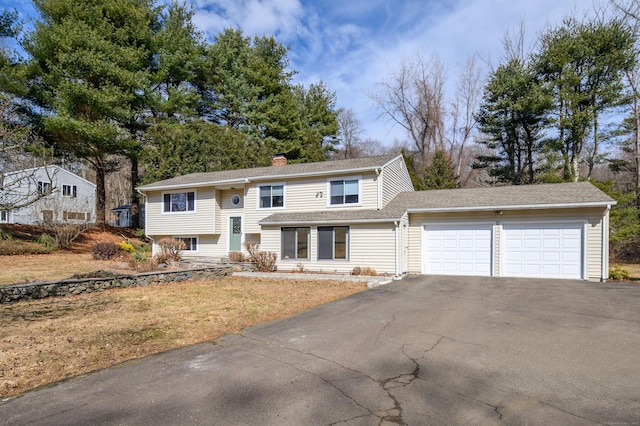 split foyer home featuring roof with shingles, driveway, a chimney, and an attached garage