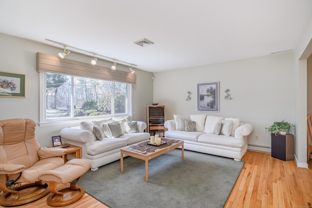 living area featuring a baseboard heating unit, light wood finished floors, visible vents, and track lighting