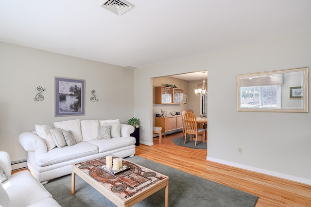 living area with baseboards, visible vents, wood finished floors, an inviting chandelier, and a baseboard heating unit