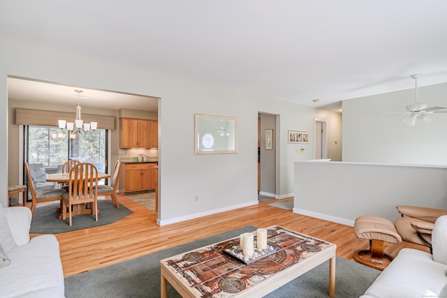 living room featuring light wood-type flooring, baseboards, and ceiling fan with notable chandelier