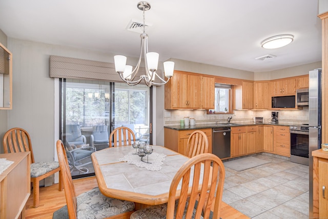 kitchen with appliances with stainless steel finishes, a sink, an inviting chandelier, pendant lighting, and backsplash