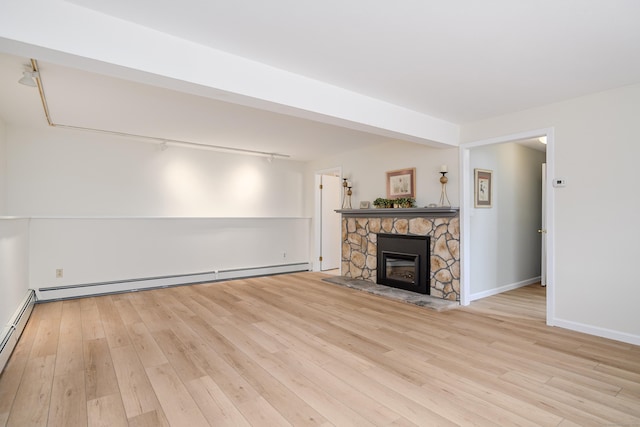 unfurnished living room with a baseboard radiator, baseboards, wood finished floors, and a stone fireplace