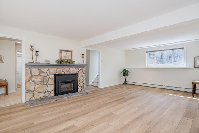 living room with a stone fireplace, a baseboard heating unit, wood finished floors, baseboards, and stairway