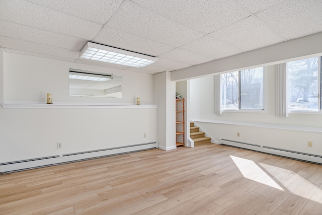 unfurnished room with stairs, a baseboard radiator, wood finished floors, and a paneled ceiling