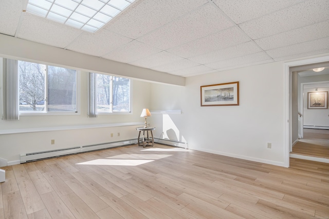 empty room featuring a paneled ceiling, a baseboard radiator, baseboards, and light wood-style flooring