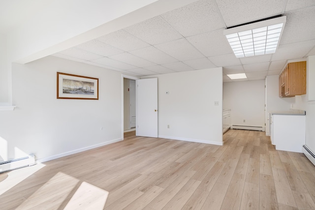 finished basement with a paneled ceiling, light wood finished floors, baseboards, and baseboard heating