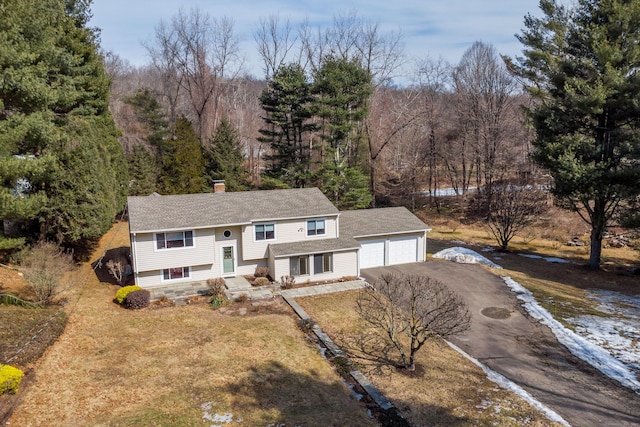 split foyer home featuring aphalt driveway, an outbuilding, a chimney, a view of trees, and a garage