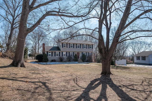 colonial inspired home featuring a chimney and a front lawn