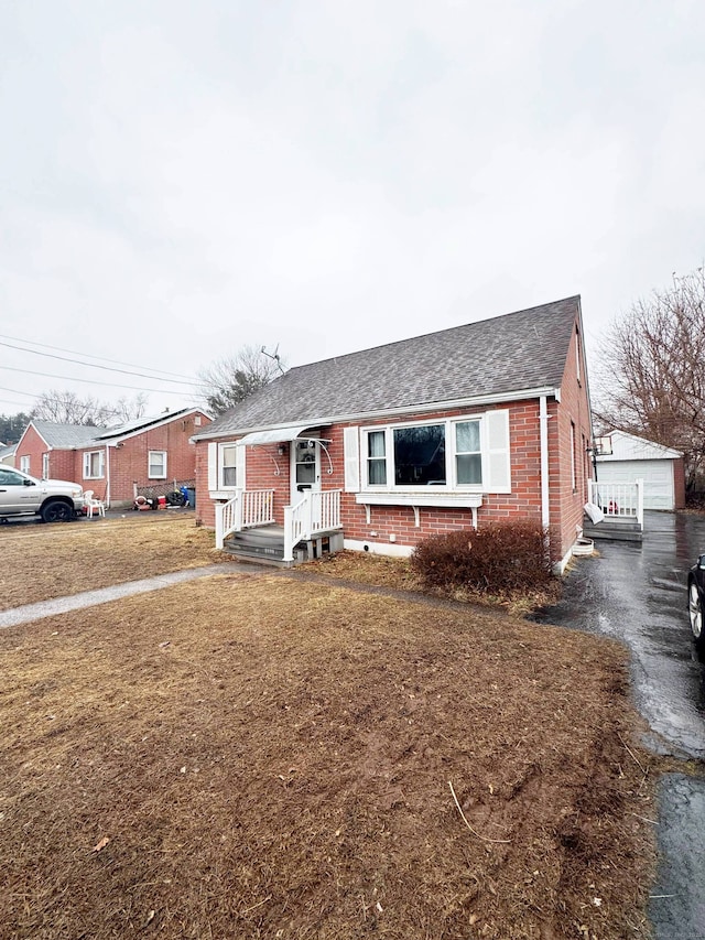 view of front of house with brick siding, a detached garage, a front lawn, roof with shingles, and an outdoor structure