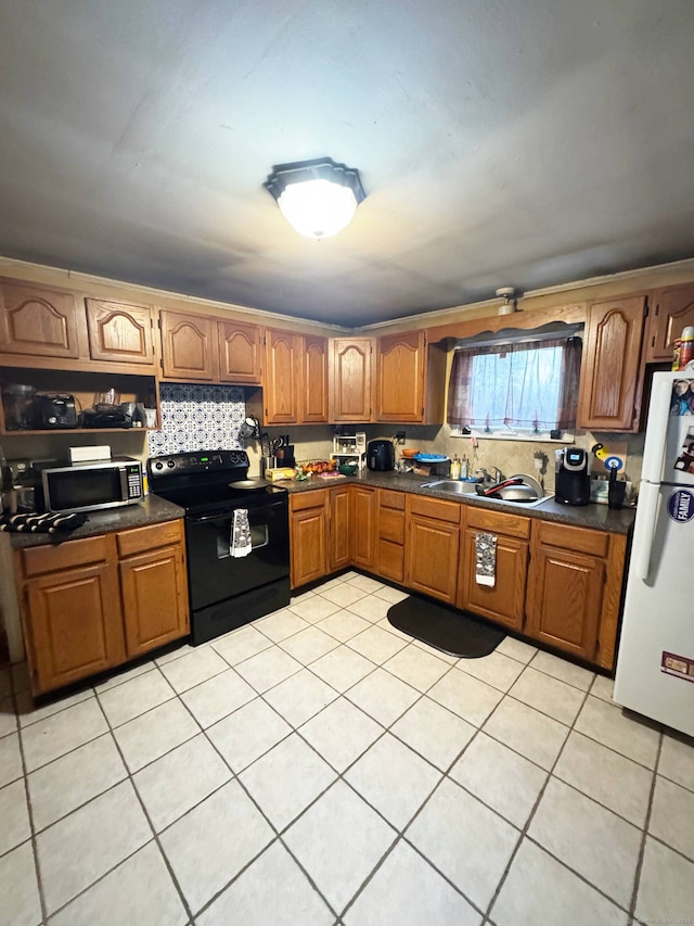 kitchen with dark countertops, black range with electric cooktop, freestanding refrigerator, brown cabinetry, and a sink