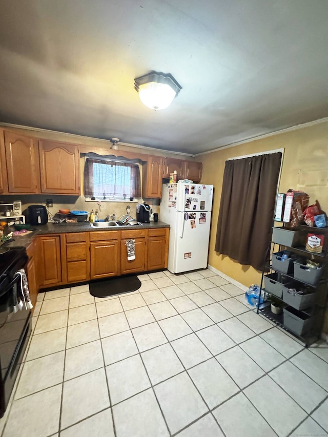 kitchen with light tile patterned floors, brown cabinetry, electric range, freestanding refrigerator, and dark countertops