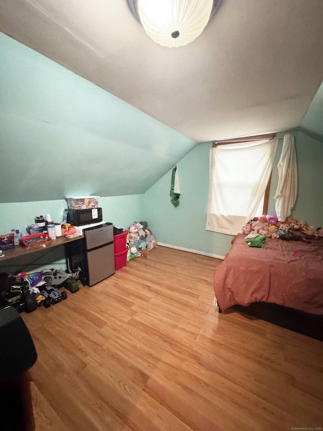 bedroom featuring vaulted ceiling, freestanding refrigerator, baseboards, and wood finished floors