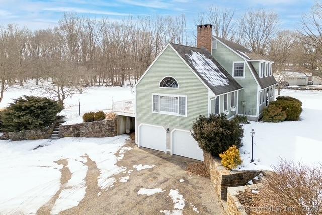 view of snow covered exterior featuring a garage, aphalt driveway, and a chimney