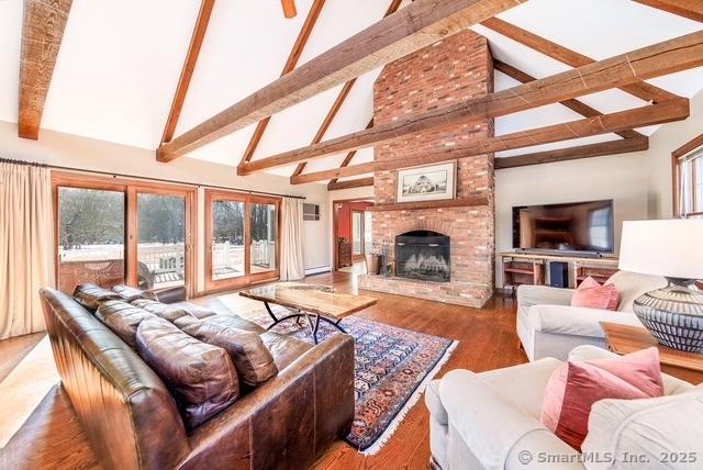 living room featuring high vaulted ceiling, a fireplace, wood finished floors, and beam ceiling