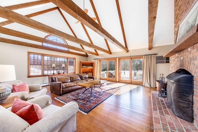 living area with high vaulted ceiling, wood finished floors, baseboard heating, a brick fireplace, and beamed ceiling