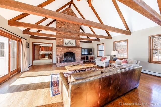 living area featuring a baseboard radiator, a brick fireplace, wood finished floors, high vaulted ceiling, and beamed ceiling