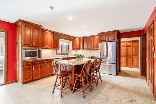 kitchen featuring a kitchen breakfast bar, a center island, light stone countertops, stainless steel appliances, and backsplash