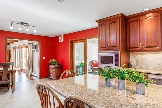 kitchen featuring light stone counters, a baseboard radiator, stainless steel microwave, and tasteful backsplash