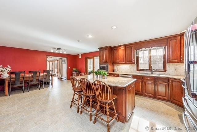 kitchen with a center island, brown cabinets, a breakfast bar area, freestanding refrigerator, and a sink