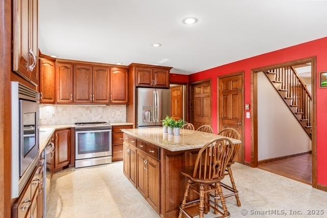 kitchen with stainless steel appliances, a center island, a kitchen breakfast bar, decorative backsplash, and brown cabinets