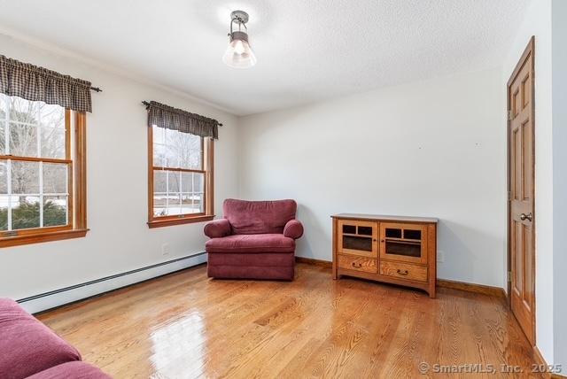 living area featuring a textured ceiling, a baseboard radiator, wood finished floors, and baseboards