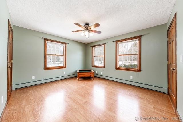 empty room with light wood-style flooring, a baseboard heating unit, baseboard heating, and a textured ceiling