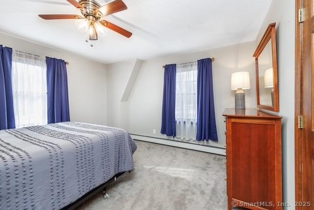 bedroom with carpet, multiple windows, a baseboard heating unit, and ceiling fan