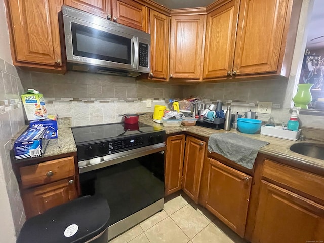 kitchen featuring light tile patterned floors, electric range, backsplash, brown cabinets, and stainless steel microwave