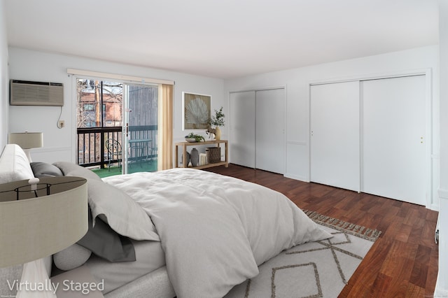 bedroom with access to exterior, dark wood finished floors, two closets, and a wall mounted air conditioner