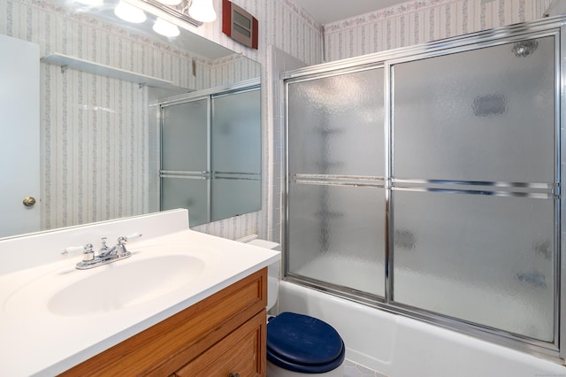 bathroom featuring toilet, wallpapered walls, combined bath / shower with glass door, and vanity