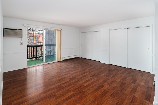 unfurnished bedroom featuring a wall unit AC, a baseboard radiator, dark wood-style flooring, and multiple closets