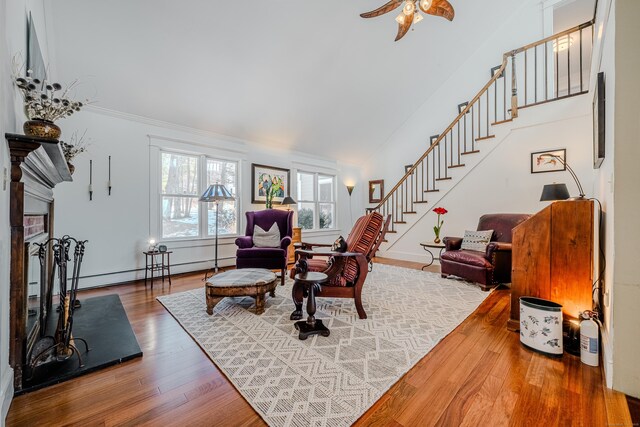 living area featuring a fireplace with raised hearth, lofted ceiling, wood finished floors, stairs, and baseboard heating