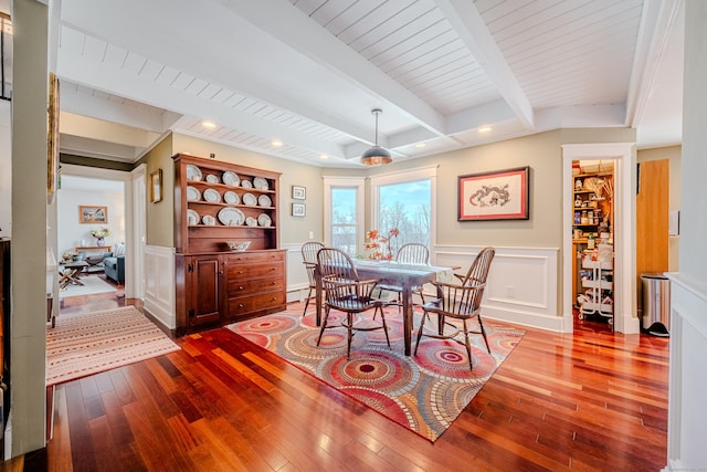 dining space with a wainscoted wall, dark wood-type flooring, beamed ceiling, and a decorative wall