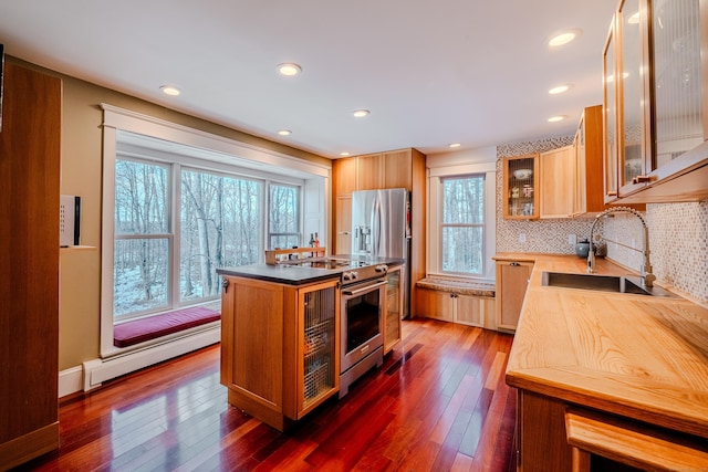 kitchen with a baseboard heating unit, dark wood-style flooring, a sink, appliances with stainless steel finishes, and decorative backsplash