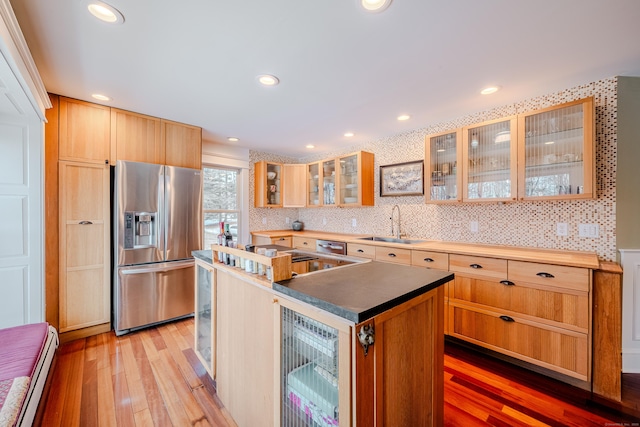 kitchen featuring stainless steel fridge with ice dispenser, light wood-style flooring, a kitchen island, baseboard heating, and a sink