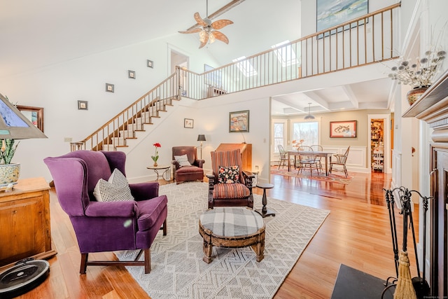 living room featuring ceiling fan, stairs, a high ceiling, and wood finished floors