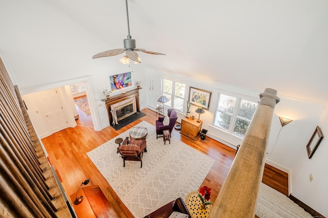 living area featuring a fireplace with flush hearth, baseboard heating, vaulted ceiling, and light wood finished floors