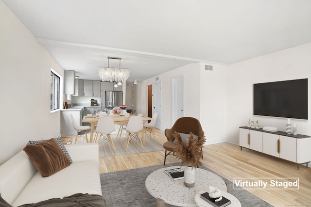 living area with light wood-style floors, visible vents, and an inviting chandelier