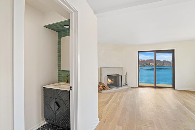 living area featuring light wood-type flooring, a high end fireplace, a water view, and baseboards