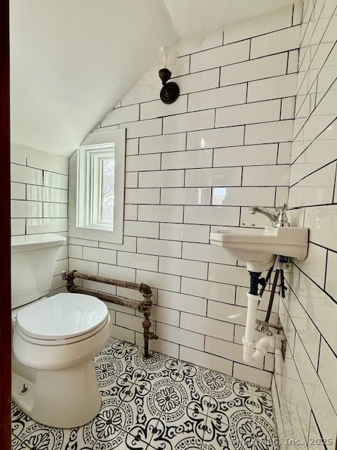 bathroom featuring toilet, vaulted ceiling, tile walls, and tile patterned floors