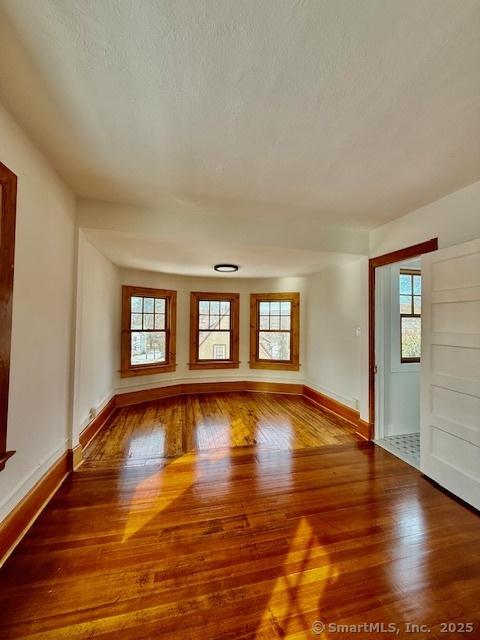 unfurnished room with a textured ceiling, hardwood / wood-style floors, and baseboards