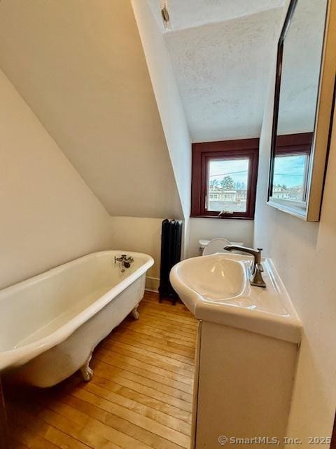 full bath with lofted ceiling, toilet, vanity, a soaking tub, and hardwood / wood-style floors